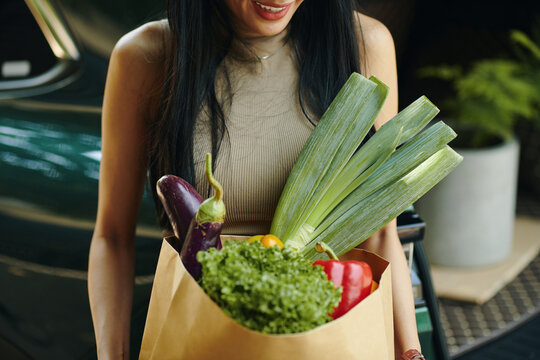 Cropped image of smiling woman holding bag of fresh groceries
