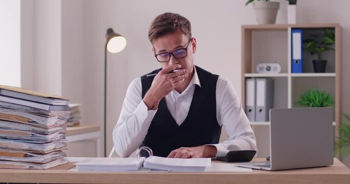 Tired young overworked business man accountant working on a laptop on his workplace with a pile of documents at office making calculations massaging eyes. Overwork, stress concept. 4k video.