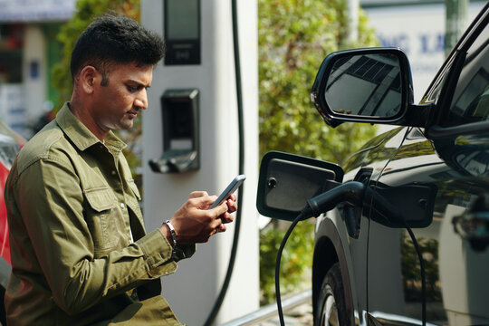 Frowning man texting when waiting for his electric car to charge