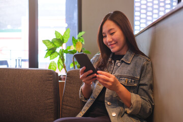 Portrait image of a young woman holding and using mobile phone in cafe - 791325337