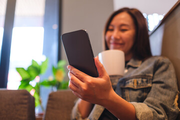 Blurred image of a young woman holding and using mobile phone while drinking in cafe