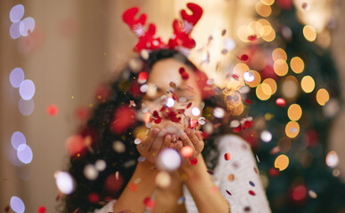 Woman, Christmas and blowing confetti for holiday celebration in home, sparkle or glitter. Female person, bokeh and festive season for winter break or xmas vacation with tree lights, fun or party