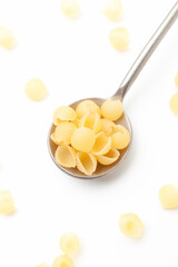 Yellow, small shell shaped pasta in iron spoon on white background