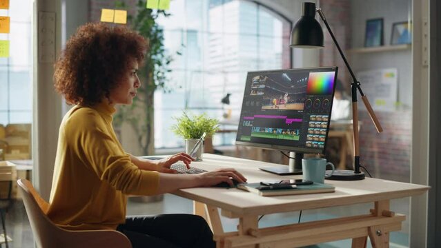Focused Female Cinematographer Works on Editing a Basketball Match Video in a Bright Modern Office Setting. Specialist Using Computer with Professional Editing Software