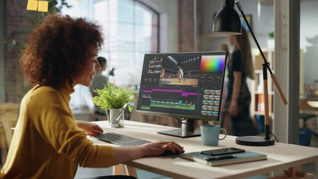 Dedicated Female Video Editor Using Computer for Editing Footage of a Basketball Tournament. Hispanic Woman Meticulously Working in a Well-Lit Creative Office Environment