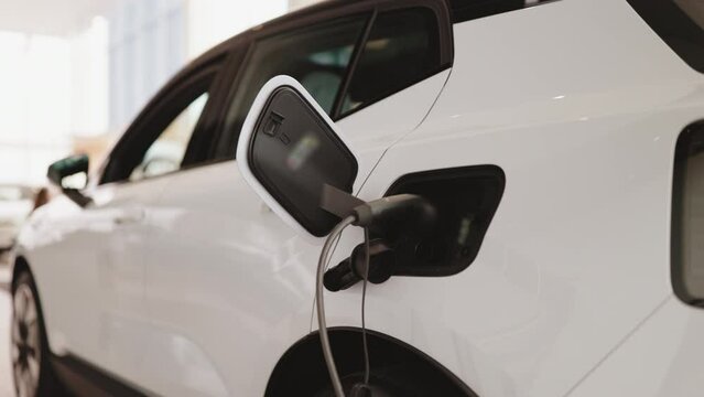 Exterior of new brand fully electric suv car in light dealership. Battery charger in white electric car based in modern showroom with panoramic windows.