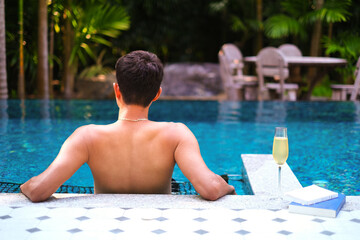 A man relaxing in a swimming pool with a glass of champagne and book at a luxury resort. Vacation, Traveller, Relax time concept. Tropical exotic holidays vacation, tourism and travel.