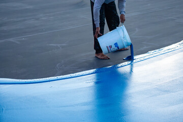 Pour the blue paint from the bucket into the floor. A man pours paint into the floor , Tennis court...
