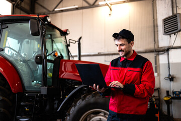 Serviceman checking tractor with diagnostic tool in workshop. Service nd maintenance of agricultural machinery.