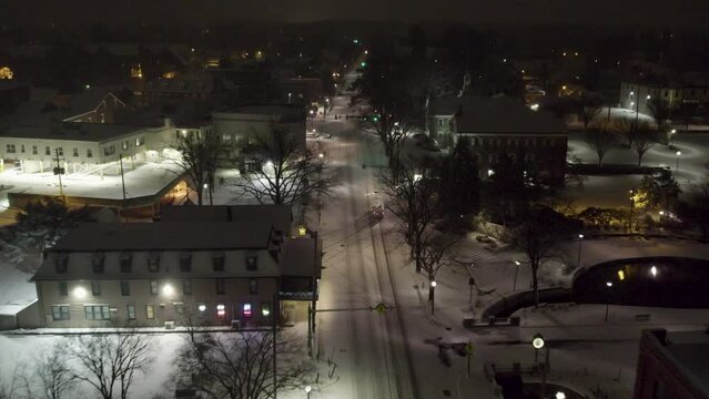 Aerial shot following a car above a snowy road in downtown Lititz at night, going south.