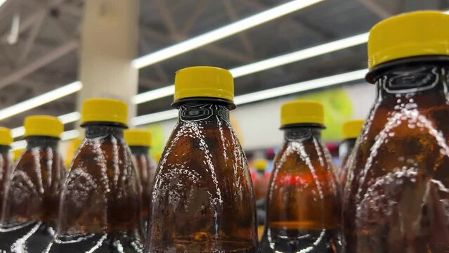 Many brown plastic bottles of drinks with yellow caps on store shelf in supermarket, warehouse