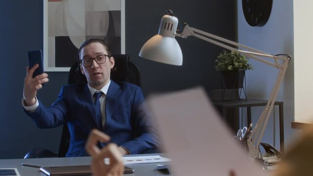 Medium over-shoulder shot of narcissistic Caucasian male corporate manager sitting at desk, preening, having video call, admiring himself, bullying and mocking subordinates workMedium over-shoulder sh