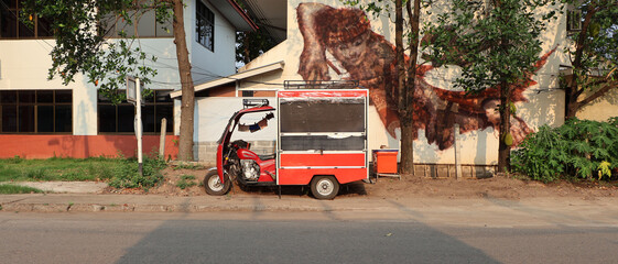 A red tuk tuk was parked on the footpath near the building.