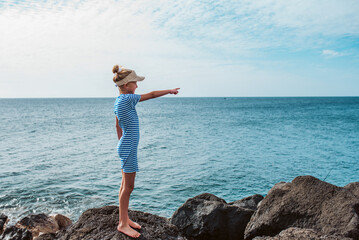 Side view of girl pointing at someting on sea. Blonde girl in dress enjoying vacation in Canary...