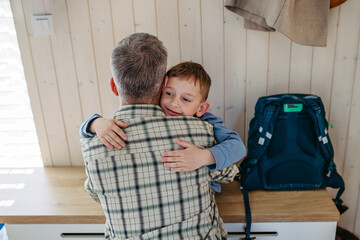 Father helping son get ready for kindergarten, preschool. Hugging, embracing. Putting coat, shoes on, handing lunchbox with snacks.