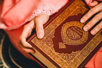 The hand of a woman in prayer clothes holds the Quran on the prayer cloth.