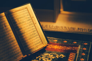 The Quran is opened for reading and placed on a prayer mat and has the golden glow of fire....