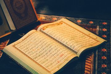 The Quran is opened for reading and placed on a prayer mat and has the golden glow of fire....