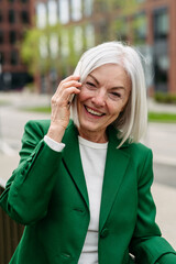 Portrait of mature businesswoman making phone call on smartphone, going home from work. Beautiful older woman with gray hair on city street.
