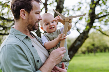 Baby and father holding wind turbine model, outdoors in park. Concept of renewable wind energy,...