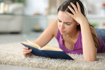 Sad woman reading a paper book on a carpet at home