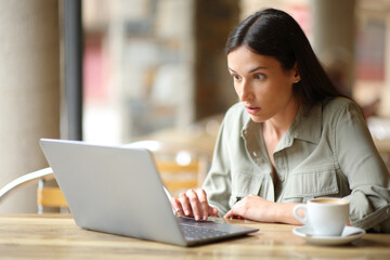Stunned woman checking news on laptop in a bar