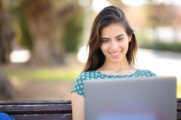 Happy student using laptop sitting in a park