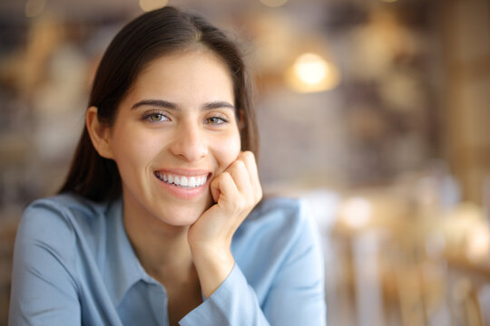 Happy woman with perfect smile posing looking at you in a bar
