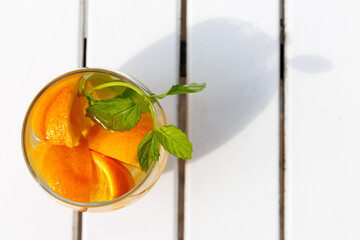 Citrus and mint leaves infused water, cocktail, lemonade in glass. Summer iced cold drink with lemon, orange, ice and mint on white wooden striped background, copy space, top view