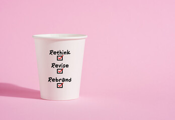 Rethink, revise and rebrand on a paper coffee cup on pink background.