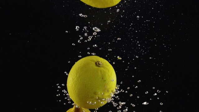 Lemons floating in the water with air bubbles on black background