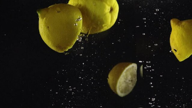 Lemon dropped in water with splash and air bubbles isolated over black background