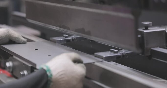 Hydraulic sheet metal bending machine. A worker bends a metal part in a machine. Metal processing