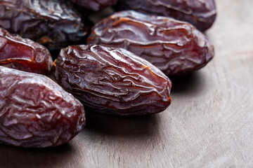 Sweet organic Medjool dates with wrinkled peel on a brown wooden surface.