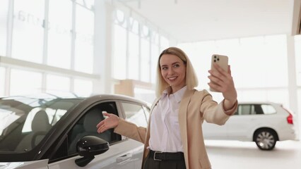 Successful businesswoman taking selfie using smartphone in car service. Happy smiling Caucasian girl buyer talking online about buying a new car.