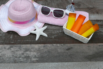 Sunscreen with beach essentials on shabby wooden board with space for text.