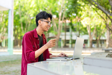 Young Asian man smiling while using laptop for working and video conference meeting at the morning. Asian man having a video call on laptop. Concept of remote and freelance 