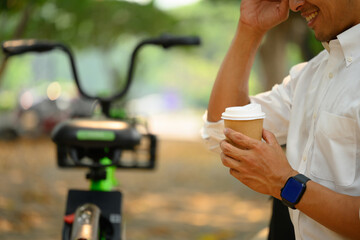 Cropped shot of relaxed businessman sitting on the park bench and drinking coffee
