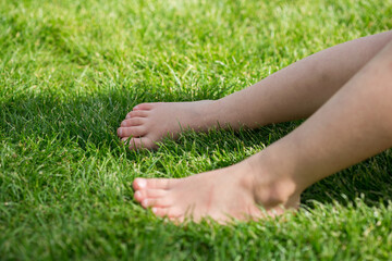 Bare feet of a child on meadow in green grass (lawn) in summer