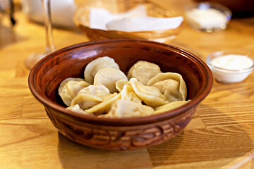 Fresh tasty dumplings in brown carved clay bowl with sour cream. Home comfort or restaurant menu and serving. Enjoy taste