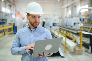 Side view of technician or engineer with headset and laptop standing in industrial factory