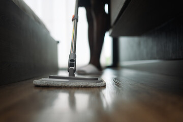 Closeup shot of man wiping wooden floor with a microfiber mop. Housekeeping concept