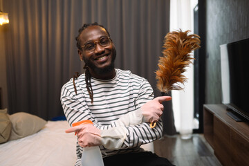 Portrait of 30s African guy holding a feather duster ready for cleaning his apartment