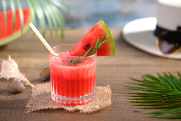Freshly watermelon juice in glasses and palm leaf on wooden table. Refreshing summer drink concept