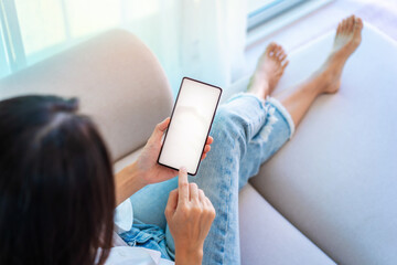 Young Asian woman relaxing and using mobile phone on a sofa at home in the morning