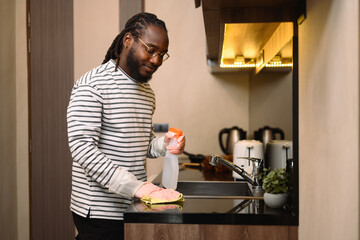 Happy young African man wearing protective glove wiping counter top in the kitchen