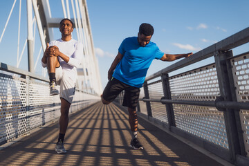 Two african-american friends are exercising on the bridge in the city. They are warming up for jogging. - 791405932