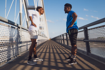 Two african-american friends are exercising on the bridge in the city. They are warming up for jogging.