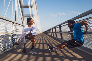 Two african-american friends are exercising on the bridge in the city. They are warming up for jogging. - 791405976