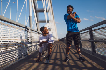 Two african-american friends are exercising on the bridge in the city. They are warming up for jogging. - 791405980